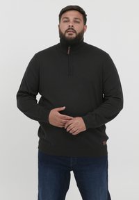 Must mustriga must-hari sahtel kootiga ja soonikkohtaga, valmistatud pehmest kangast. Tal on väike pruun nahast logo silt allääres. Kandmine siniste teksadega.