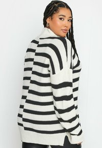 Gestreifter Strickpullover in Schwarz und Weiß mit hohem Kragen, lockerer Passform und seitlichen Schlitzen, ausgestattet mit texturiertem Garn und gerippten Bündchen.