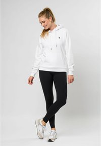 Hvit hettegenser med snøring og kengurulomme, sammen med svarte leggins og lyse sneakers. Glatt stoff og avslappet passform.