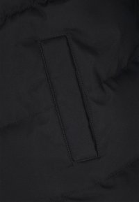 Zwarte stof met een verticale, gestikte rechthoekige zakopening, voorzien van horizontale doorgestikte naden op het textieloppervlak.