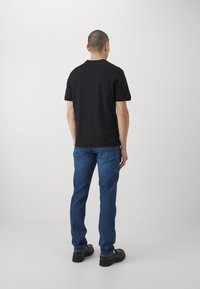 Schwarzes Baumwoll-T-Shirt mit kurzen Ärmeln, kombiniert mit blauen Jeans. Die Passform ist regular, und das Outfit weist minimale Details auf.