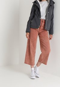 Szara kurtka z kapturem wyściełana białą, miękką podszewką, zestawiona z szerokimi jeansami w wyblakłym różowym kolorze oraz białymi trampkami. Minimalistyczny design, bez wzorów.