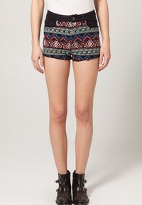 Shorts negros y estampados que presentan un diseño tribal en rojo, azul y blanco, con dobladillo deshilachado y un cierre de botones en la parte frontal. Combinados con botas negras hasta el tobillo.
