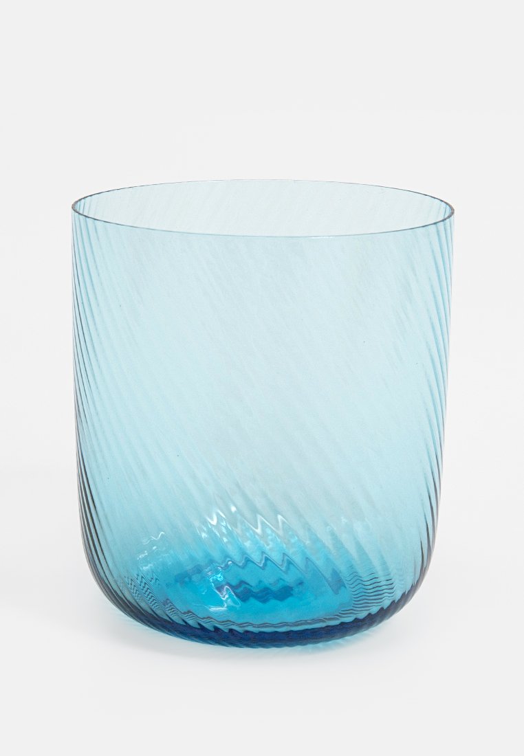 Vaso de vidrio azul translúcido con sutil textura acanalada diagonal, forma cilíndrica ancha y base redondeada sobre un fondo blanco.