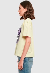 Lys gul kortærmet t-shirt med et lilla grafisk design på fronten. Løs pasform med rund halsudskæring og blød bomuldsstruktur.