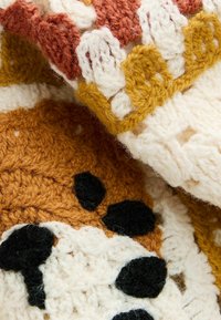 Horgolt takaró meleg barna, világosbézs és mustár színekkel, texturált mintákkal és fekete kiegészítőkkel. Puha, hurkolt fonalból készült szerkezet.