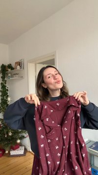 Robe bordeaux à encolure dégagée, manches courtes, ornée de motifs de nœuds blancs et de poches avant. Le tissu semble doux et texturé.