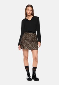 Schwarze Bluse mit langen Ärmeln kombiniert mit einem Minirock im Leopardenmuster. Das Model trägt schwarze Stiefeletten mit dicken Sohlen und knielange Socken.