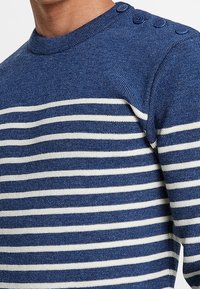 Blå och vit randig tröja med strukturstickning, med knappar på axlarna och design med rund halsringning.