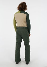 Aansluitend long sleeve top in bruin en groen, gecombineerd met donker groene, losse broek. Het materiaal lijkt soepel met een matte afwerking.