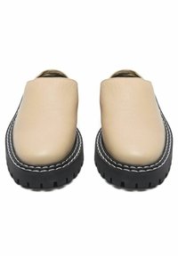 Paire de chaussures beige à enfiler avec semelles épaisses noires et coutures blanches autour des bords, vues de face.