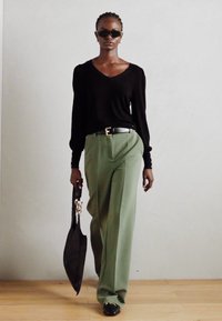 Maglia nera a maniche lunghe, pantaloni verdi a gamba larga, cintura nera con fibbia dorata, borsa nera oversize, occhiali da sole scuri, texture liscia, stile minimalista.