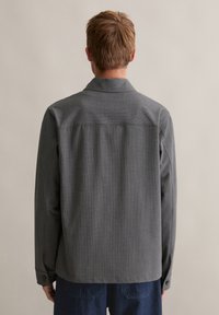 Szara koszula z tkaniny o splocie, z kołnierzykiem, długimi rękawami i mankietami na guziki. Charakteryzuje się subtelną fakturą oraz prostym tyłem bez widocznych wzorów.