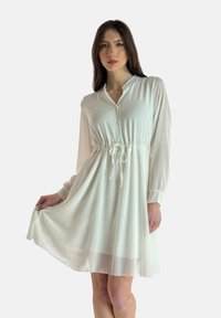 Vestido blanco de manga larga con cuello de botonadura y cintura con cordón. Tela sedosa con una falda vaporosa de longitud a la rodilla.