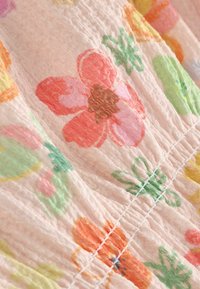 Primer plano de tela arrugada de color rosa pálido con estampados florales multicolores y costuras visibles en un patrón diagonal.