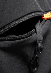 Czarna torba z tkaniny z pomarańczowym uchwytem zamka, widocznym paskiem i metalowym klipsem. Miękka tekstura i prosty design.