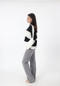 Maglione oversize a righe bianche e nere con lavorazione a maglia texturizzata, abbinato a jeans grigi chiari a zampa e sandali trasparenti con tacco alto.