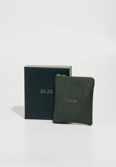 Roheline sametist tõmblukuga klamber kuldse "JIA.JIA" logo ja tumeroheline kingituskast. Pehme tekstuur ja kompaktne ruudukujuline vorm.