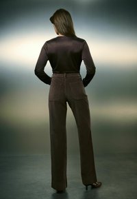 Pantalones de pana marrón de pierna ancha con dos bolsillos traseros, combinados con una parte superior ajustada de color oscuro. Textura suave, diseño formal y silueta ajustada.