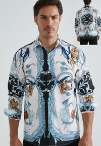 Chemise à manches longues pour homme en blanc et noir, avec des motifs floraux et géométriques bleus, col boutonné et tissu texturé.