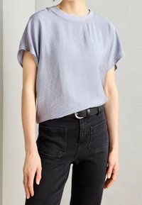 Světle modrý top s krátkým rukávem vyrobený z texturované látky, v kombinaci s černými džíny z denimu s zadními kapsami a černým opaskem se stříbrnou sponou.