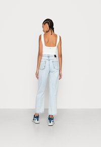 Top branco sem mangas com costas em quadrado, combinado com jeans de cintura alta azul claro e ténis azuis, rosas e pretos. Fundo liso.