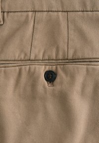 Beige fabric with a diagonal stripe pattern. Features a black button at the center with a small loop, emphasizing texture and detail.