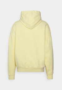 Sudadera con capucha amarilla, material de algodón suave, corte relajado, puños y dobladillo acanalados. La vista trasera muestra una textura suave y la forma de la capucha.