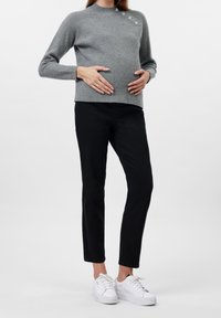 Suéter de punto gris acanalado con tres botones decorativos, combinado con pantalones negros ajustados y zapatillas blancas. El suéter tiene un cuello alto.