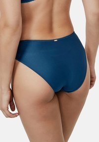 Culotte de bikini taille haute en bleu foncé. Fabriquée dans un tissu texturé au fini lisse. Présente un subtil accent doré sur la taille.