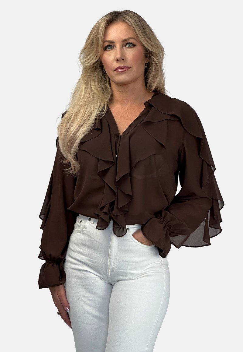 Brązowa, marszczona bluzka z lekkiego materiału z długimi rękawami, zestawiona z białymi dżinsami z wysokim stanem. Akcenty to dekolt w serek oraz rozszerzane mankiety.