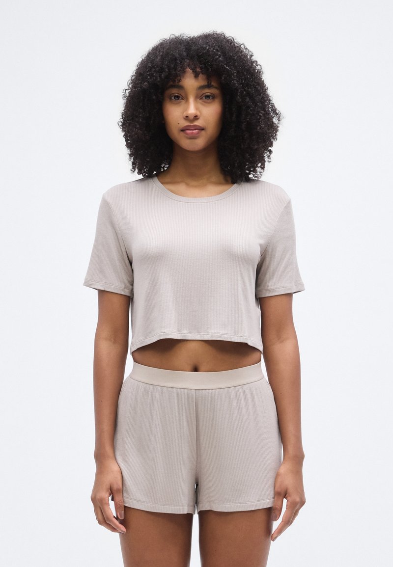 Ensemble crop top et short beige clair, en tissu côtelé. Le crop top présente des manches courtes et le short possède une taille confortable.