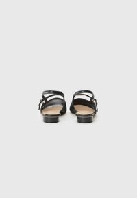 Black leather sandals with a low heel. Features an open back and crisscross ankle straps. Smooth texture with minimal detailing.