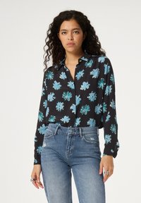 Schwarzes Langarmhemd mit blauem Blumenmuster, mit Kragen, aus leichtem Stoff und einem lockeren Schnitt, kombiniert mit hoch taillierten Jeans.
