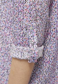 Manche d'une chemise multicolore à pois retroussée et maintenue par une patte boutonnée.