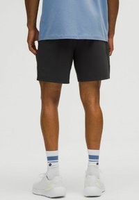 Sorte atletiske shorts med en glat tekstur, parret med hvide sko og blårandede sokker, båret med en lyseblå skjorte.