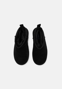 Zapatos slip-on negros hechos de suave ante con un forro mullido, punta redonda y pequeñas pestañas en la parte posterior para facilitar su uso.