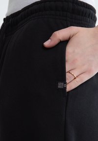 Hand met gouden ring rustend in de zak van zwarte Big Star sweatpants met elastische taille.