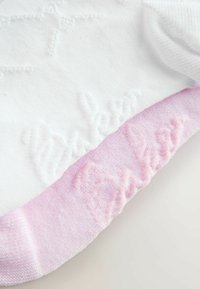 Baltā zeķe ar rozā ribošanai; augšdaļai ir teksturēts raksts. Mīksts materiāls un elastīgas malas, lai nodrošinātu ciešu piegulšanu.