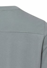 Lysegråt stof med en søm tværs over den øverste ryg og tekstureret strik på den øverste sektion og ærmerne af et beklædningsstykke.