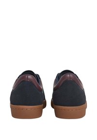 Par de zapatillas casuales de corte bajo en ante azul marino oscuro, con acentos del talón en cuero marrón y suelas de goma marrón claro, vistas desde la parte trasera.