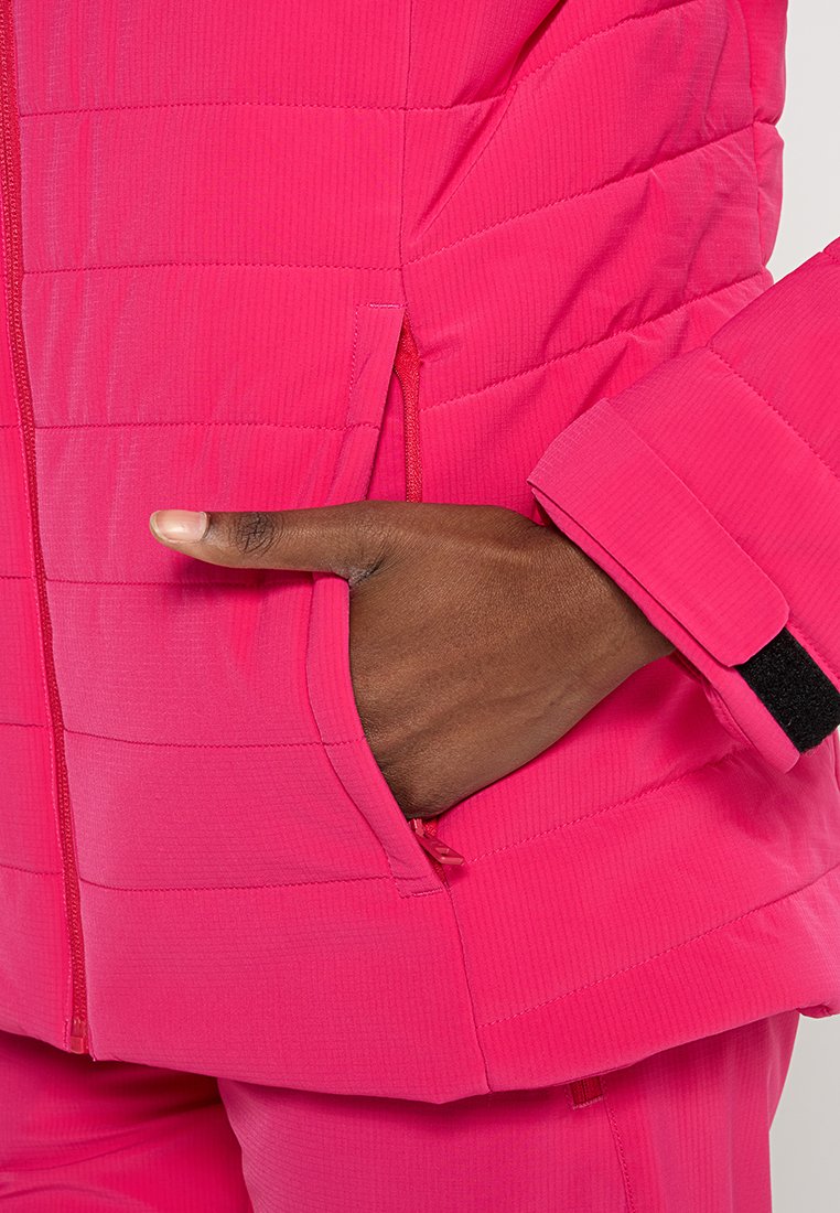 Helle pinke isolierte Jacke mit gestepptem Design und seitlicher Tasche. Der Stoff zeigt eine gerippte Textur und einen eleganten Reißverschluss mit Klettverschluss am Bund.