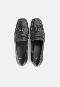 Μαύρα δερμάτινα μοκασίνια με στρογγυλεμένη μύτη, διακοσμημένα με φούντες και ραφές σε αντίθεση. Λείο υλικό με γυαλιστερό φινίρισμα.