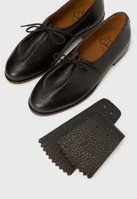 Μαύρα δερμάτινα παπούτσια με υφή, στρογγυλεμένη μύτη και λεπτά κορδόνια. Περιλαμβάνει τακούνι με την ίδια υφή και κυματιστά άκρα.