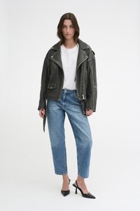 Veste de moto en cuir noir avec des accessoires en argent, t-shirt blanc, jeans bleu clair et escarpins noirs à bout pointu, se tenant sur un fond neutre.
