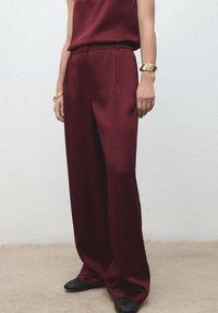 Bordeaux wijde broek van een soepele stof, voorzien van geplooide details en een hoge taille, gecombineerd met een bijpassend top en zwarte flats.