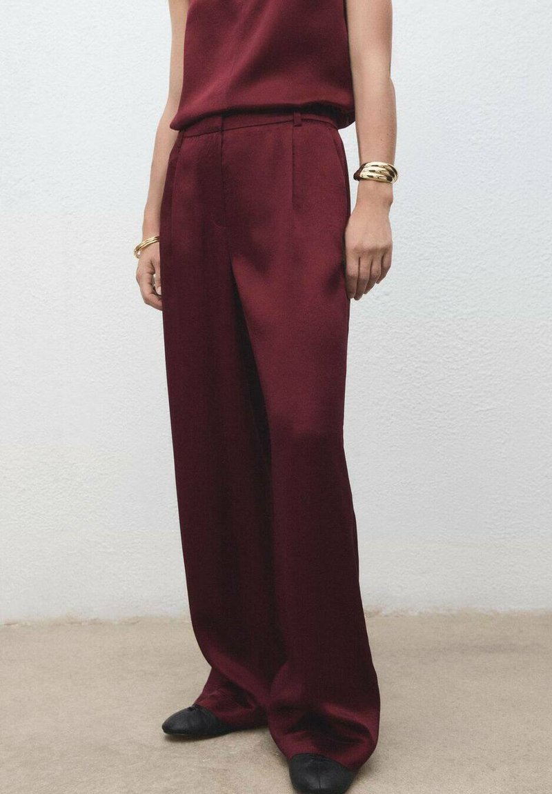 Bordeaux wijde broek van een soepele stof, voorzien van geplooide details en een hoge taille, gecombineerd met een bijpassend top en zwarte flats.