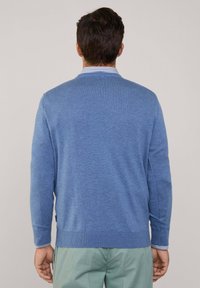 Blauwe trui gemaakt van een textuurgebreid materiaal, met een ronde halslijn en ribbelmanchetten. De zoom en manchetten hebben een subtiele gestreepte accent.