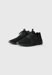 Baskets de sport noires avec tige en maille texturée, orteil renforcé, lacets contrastants et semelle rembourrée conçue pour le soutien et le confort.