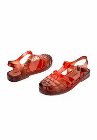 Sandalias de gel rojo translúcidas con diseño trenzado, correa ajustable en el tobillo y suela plana. Textura suave y punta redondeada para mayor comodidad.